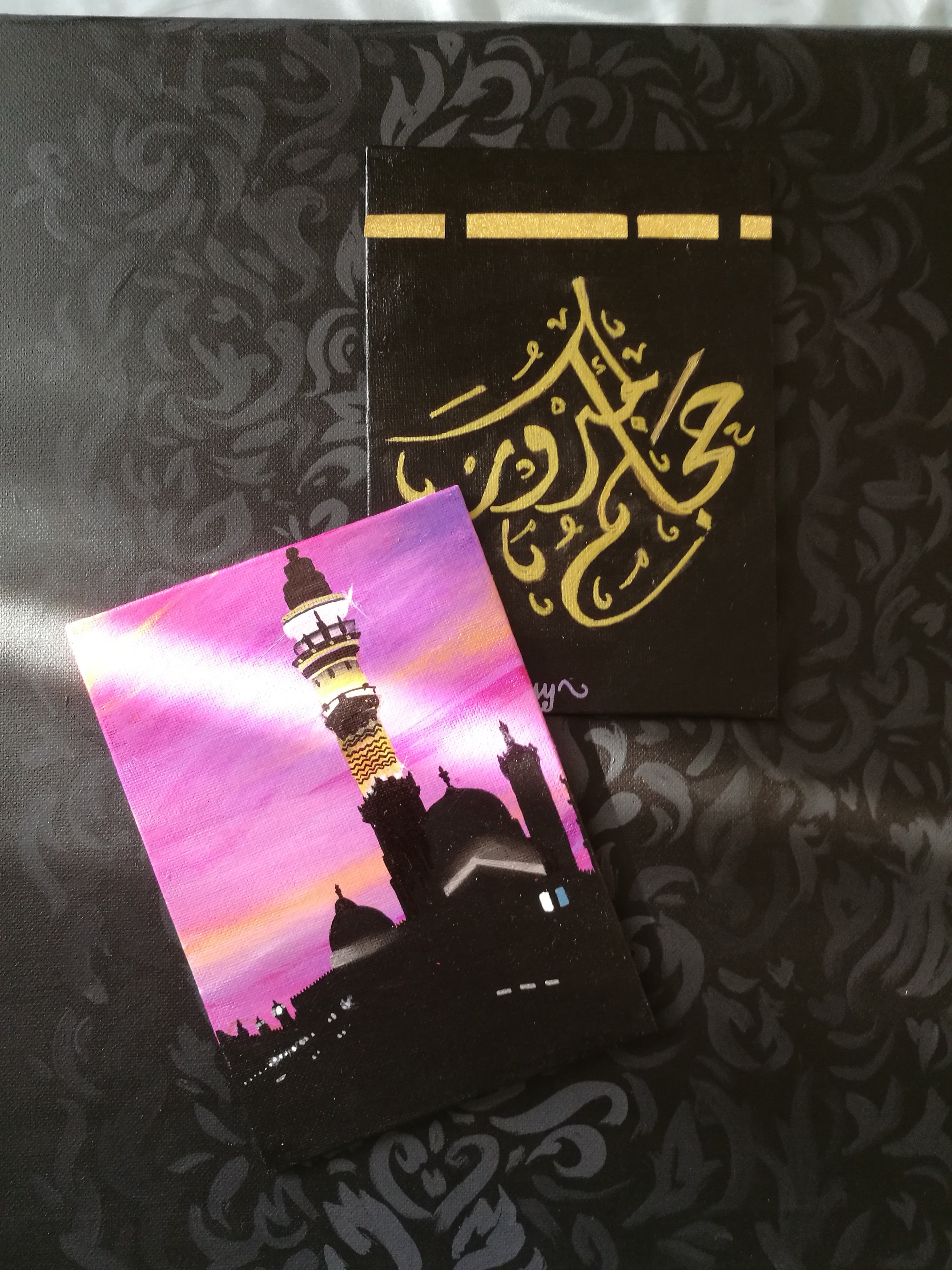 Two cards on a black patterned background, one with Arabic calligraphy and the other with a pink and purple design.
