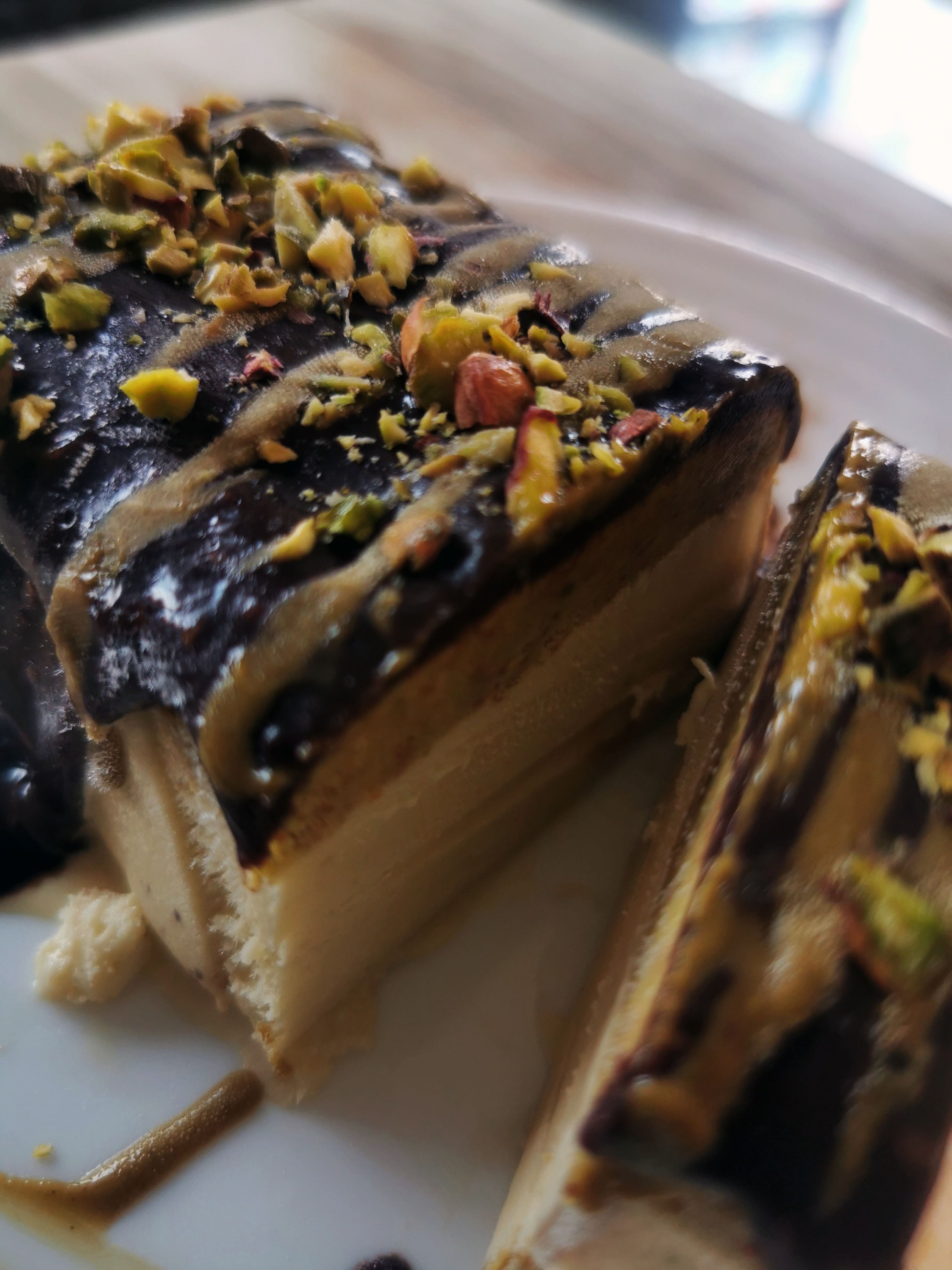 Close-up of a dessert with chocolate and pistachio toppings on a white plate.